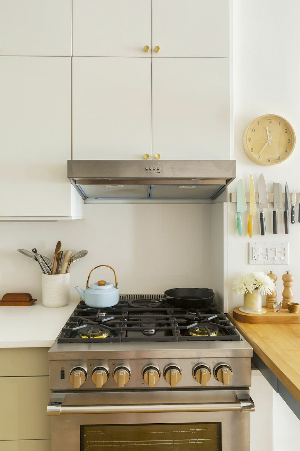 white kitchen cabinets with white countertop and stainless steel gas cooking range with brass knobs and hood after renovation 