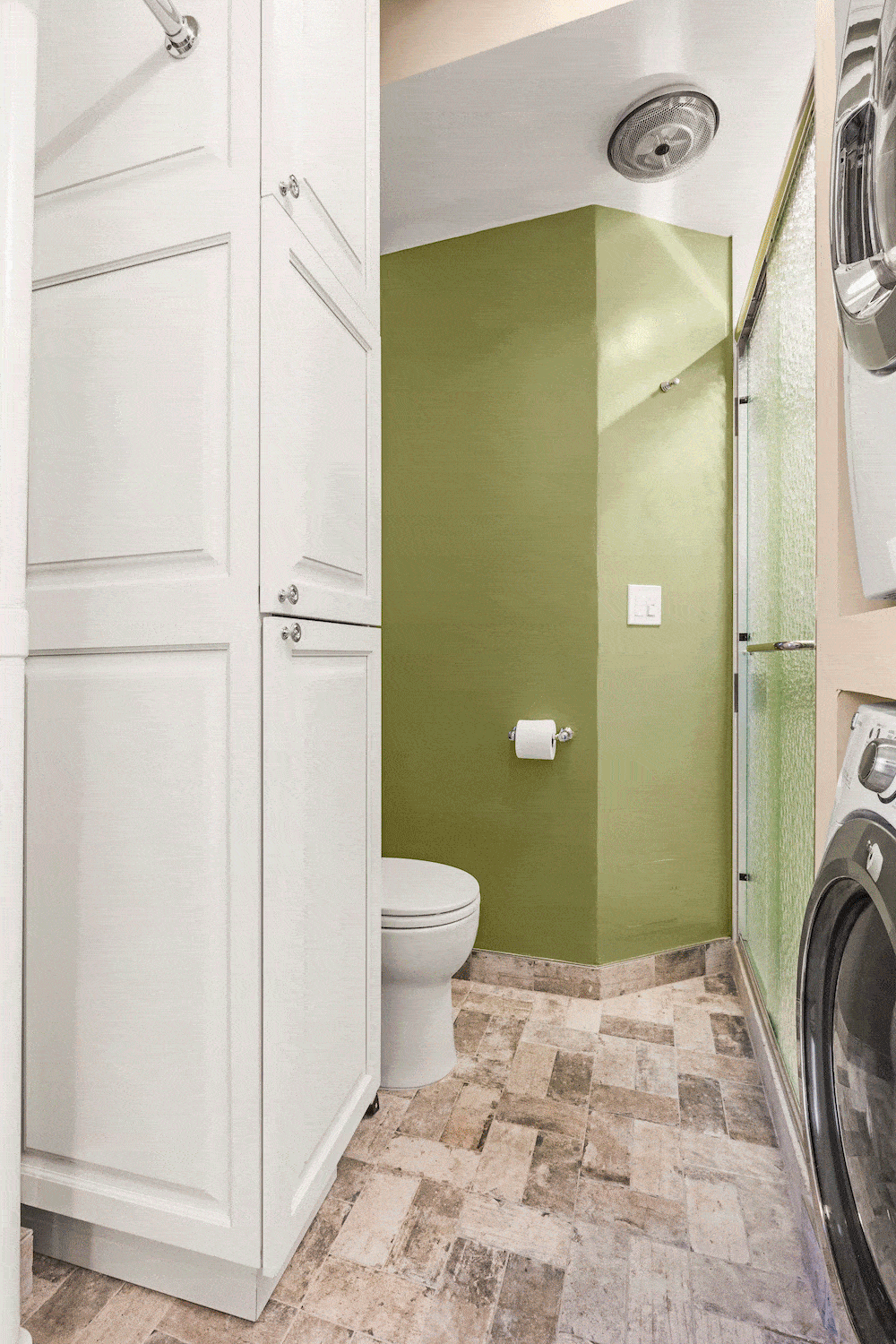 White storage cabinetry near stacked washer dryer and toilet after renovation