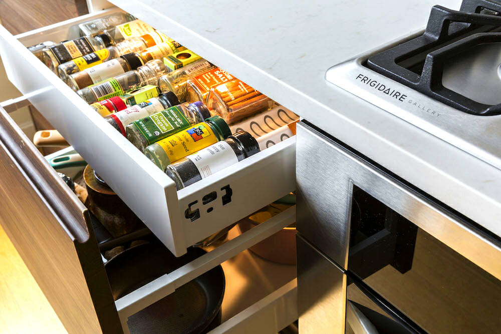pull out spice cabinets with marble countertop and next to stainless steel gas cooking range after renovation