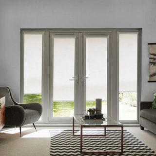 A modern living room with large glass patio doors and side windows, partially covered by white roller blinds.