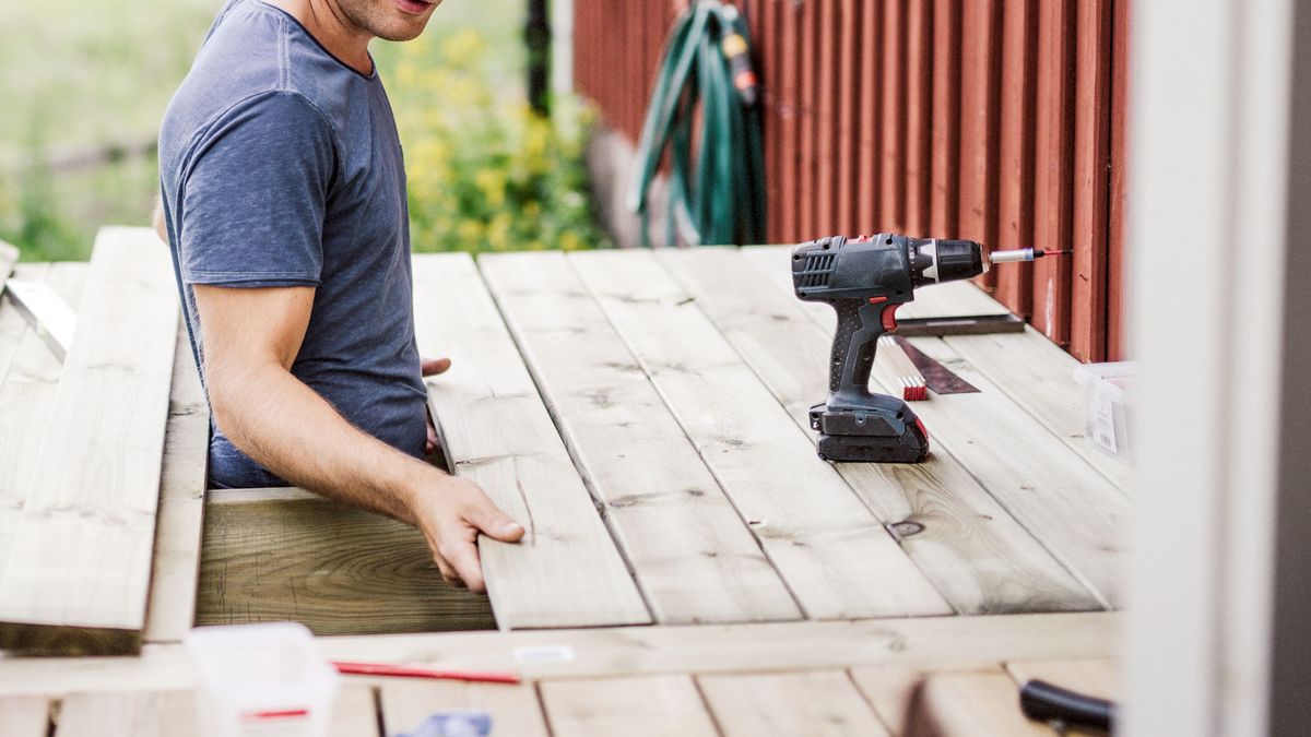 Man adding new wooden deck plank with drill next to him