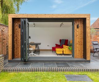 A flat roofed timber framed garden room with its bifolding patio doors opening into a lawned area