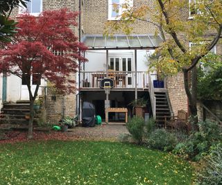 before shot of terraced brick house showing covered balcony with steps leading down to garden and basement left open below