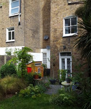 terraced brick house showing patio doors at rear and overgrown garden