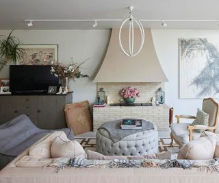 inside living room with cream brick fireplace, comfy sofas, modern white pendant tube light and ceiling spotlights