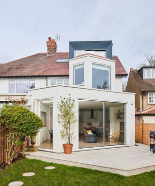 white brick living room extension set at an angle, with sliding patio doors on two sides and a smaller cube extension with large windows on top of ground floor