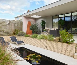 exterior of extension showing seating area and fire under roof and water feature on lower level