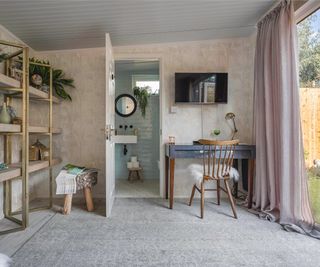 garden room with door open onto small ensuite, wooden floor with large grey rug, shelving and corner desk with tv above