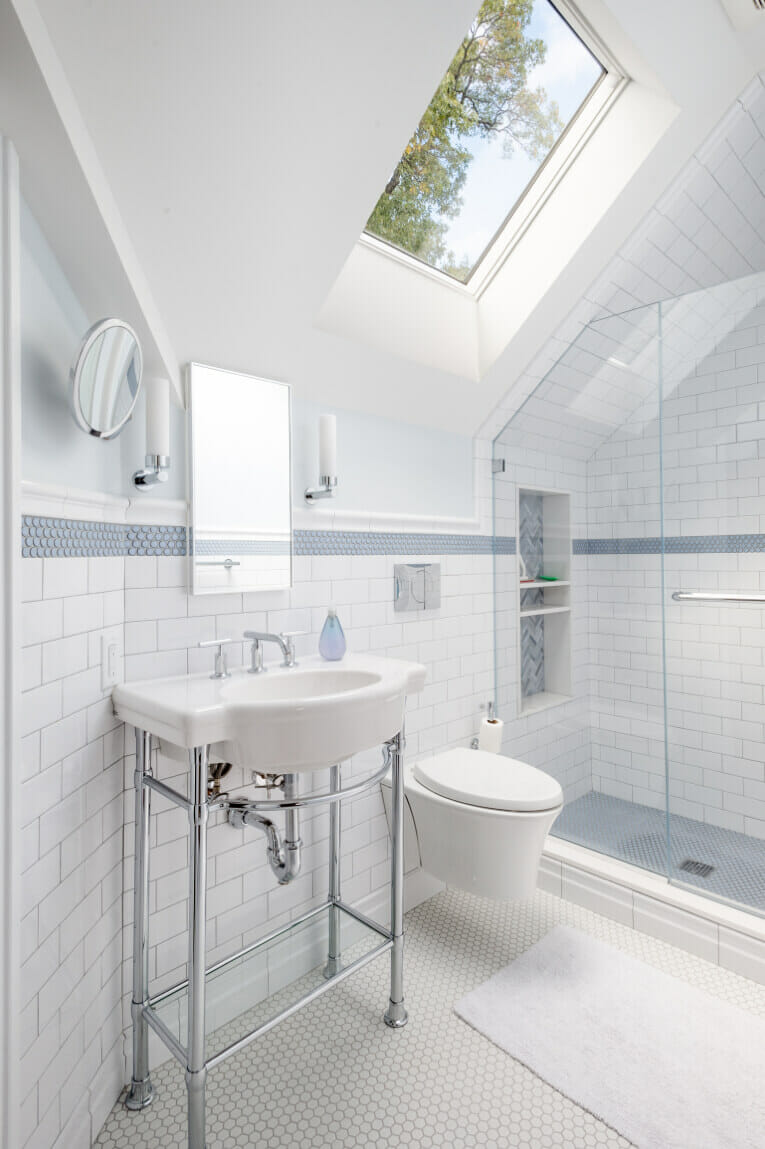 Remodeled attic bathroom with skylight, white and blue tiles, traditional vanity, and wall-mounted toilet
