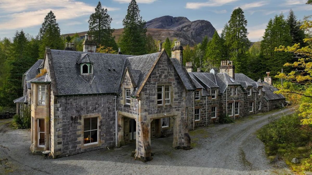 A stone lodge surrounded by forestry and a stone driveway