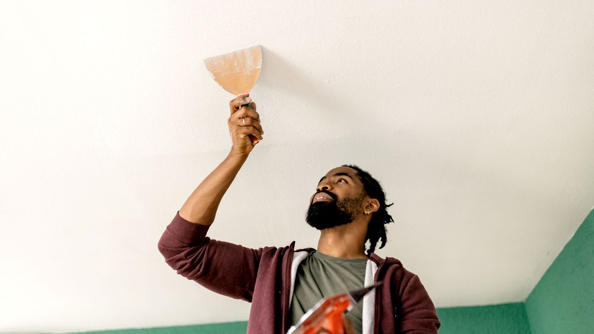 Man adding filler to hole on ceiling with wide putty knife