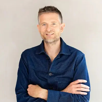male with short dark hair, short facial hair wearing dark blue denim shirt and folding his arms