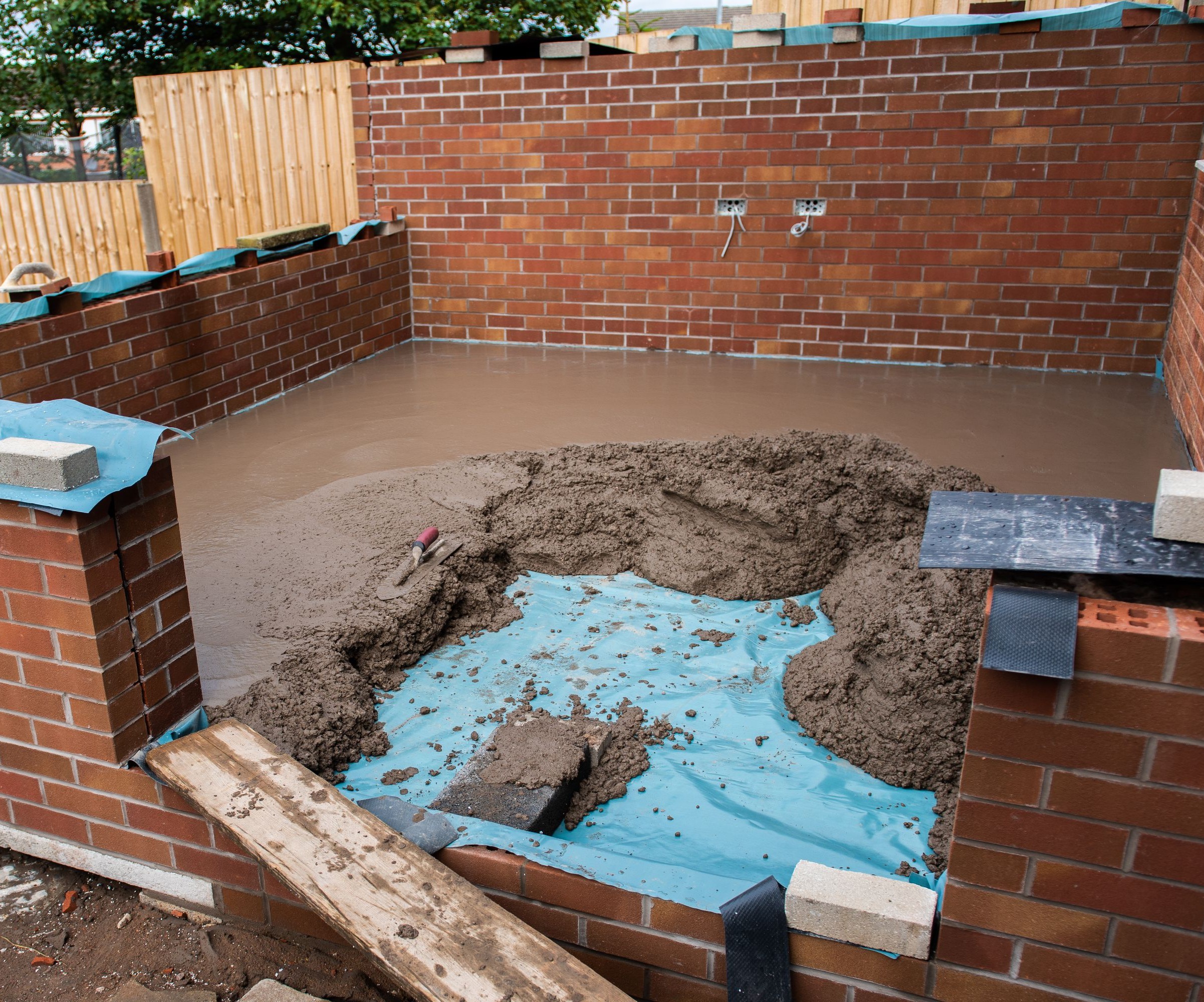 Concrete being laid over a bright blue damp proof membrane with brickwork around it