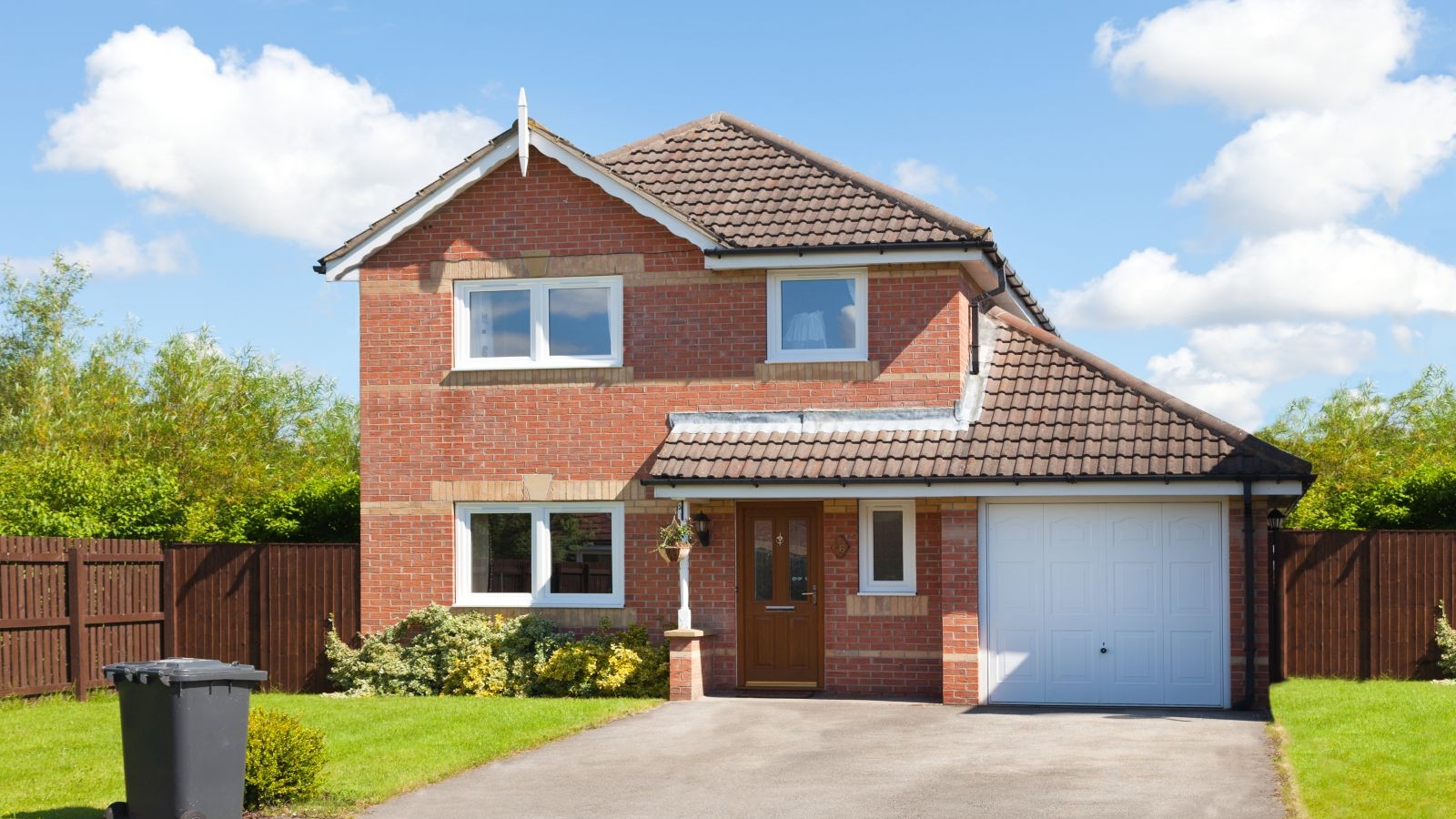 A home with red brick and a brown front door and white garage door