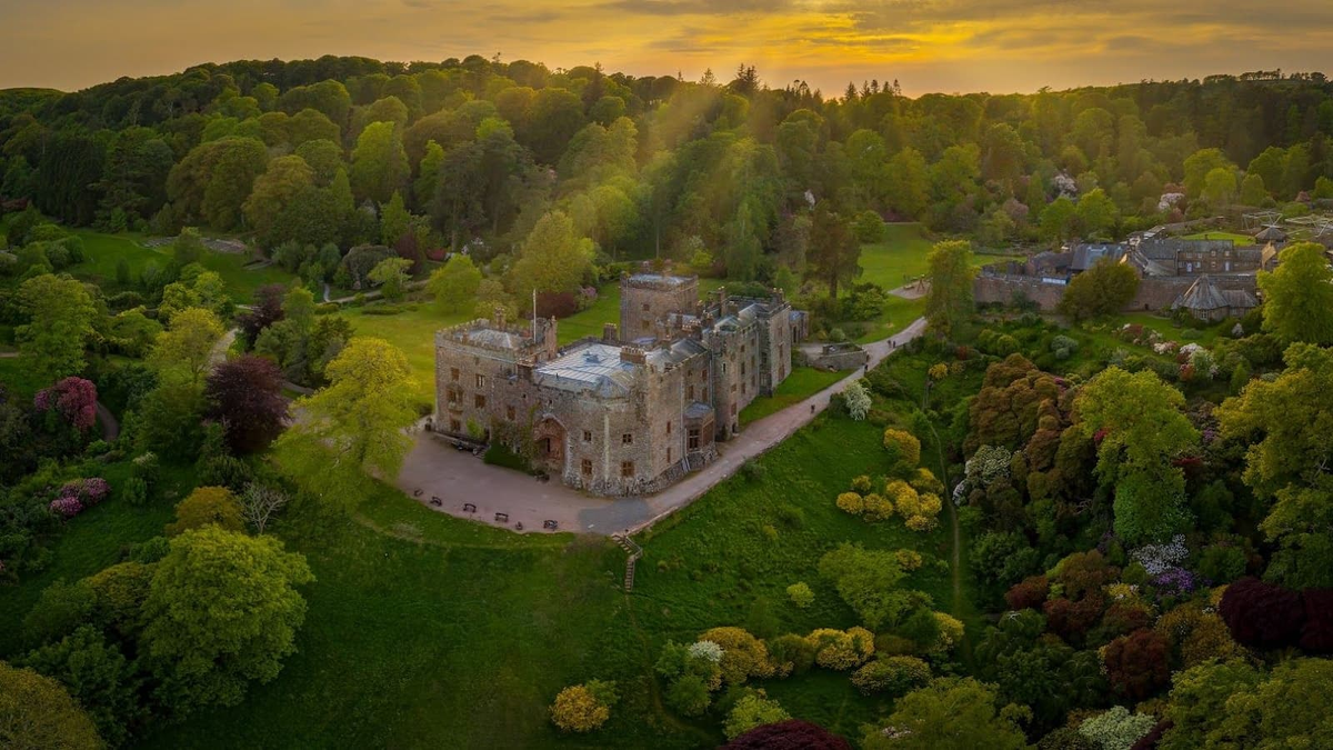 A castle with surrounding fields and trees with sunlight illuminating it