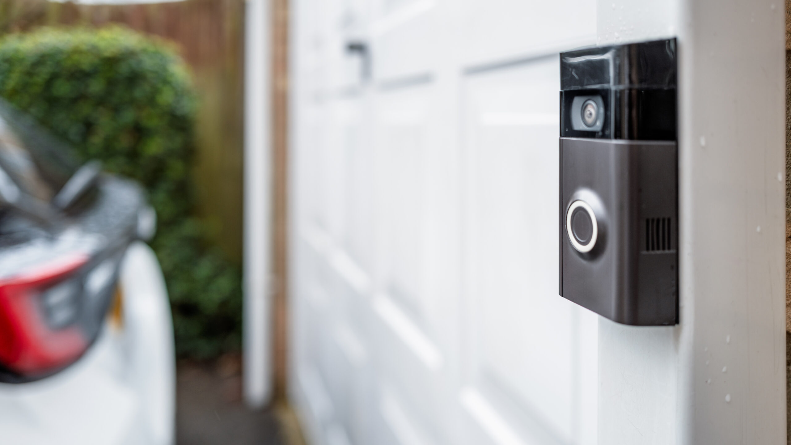 Doorbell camera mounted on wall with white garage door and back of white car beyond