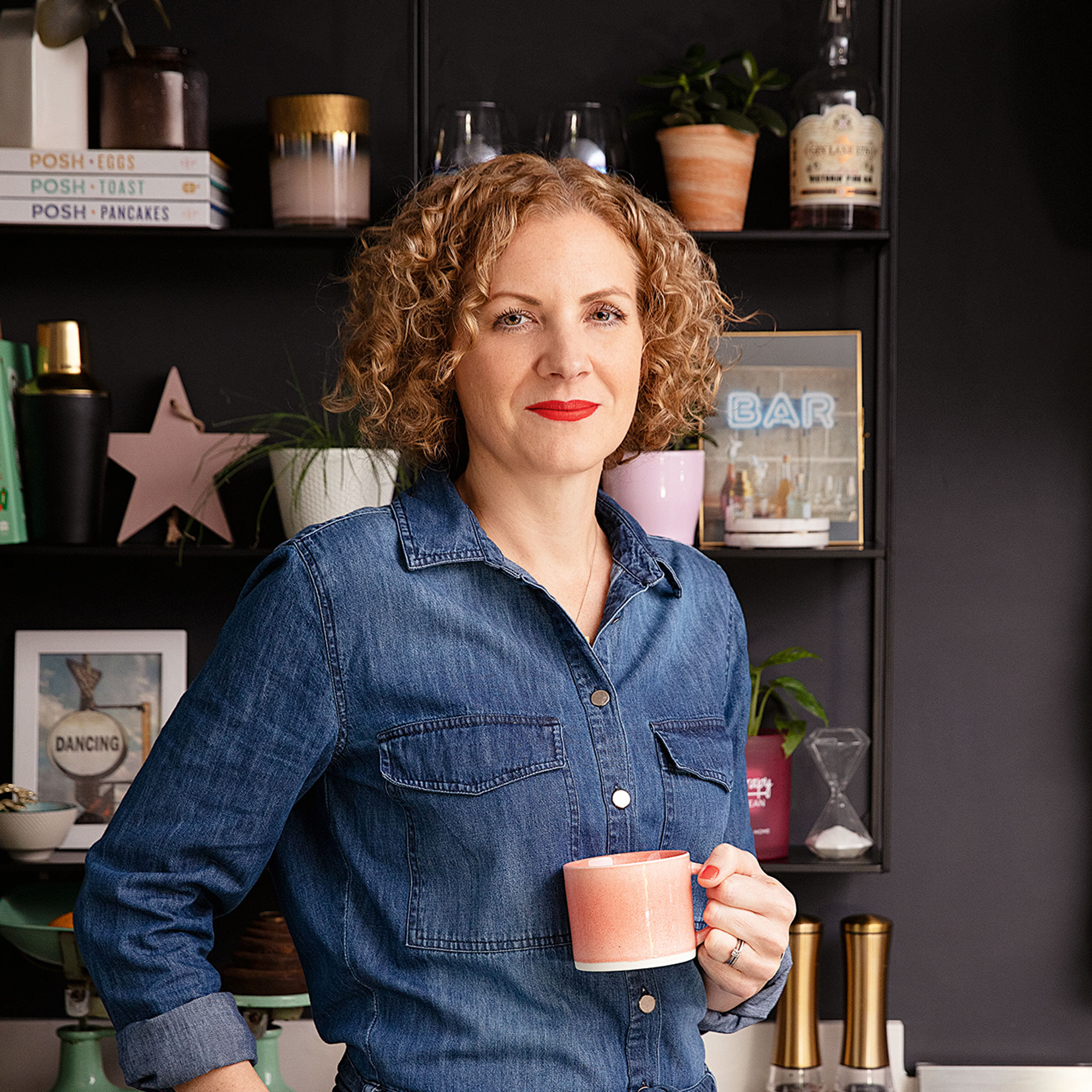 Beth Murton standing in front of open shelving and holding a pink coffee mug