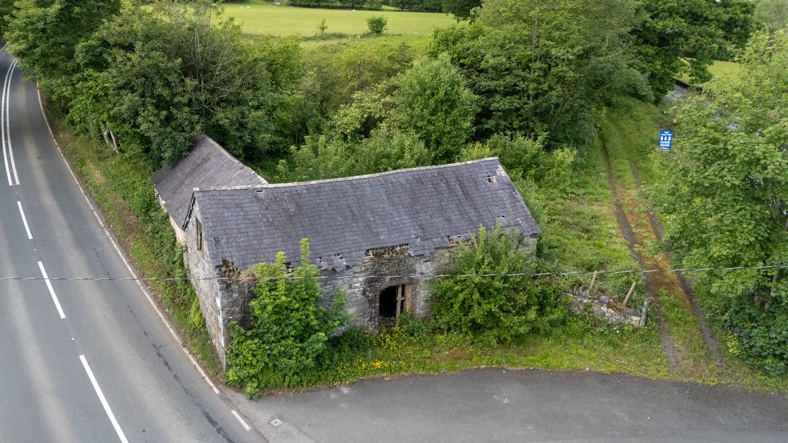 A stone barn next to a road and fields with a small driveway