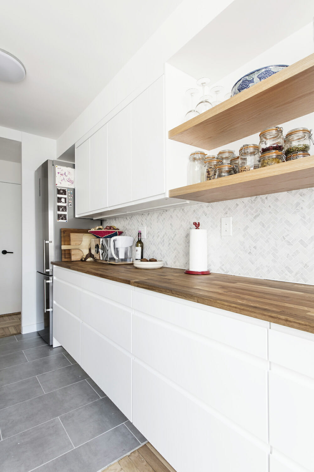 brown wooden countertop with white kitchen cabinets and open shelves on walls after renovation