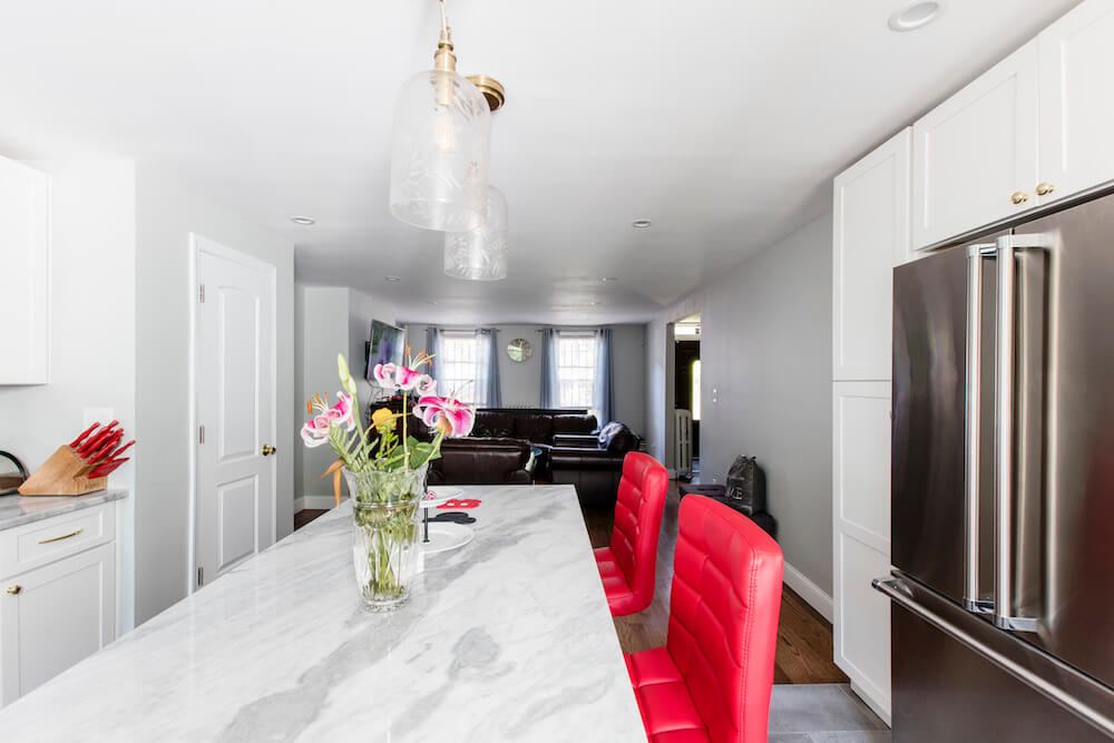 open kitchen with white cainets and white walls and island with marble countertop and stainless steel appliances and pendant lights and living room with hardwood floors after renovation