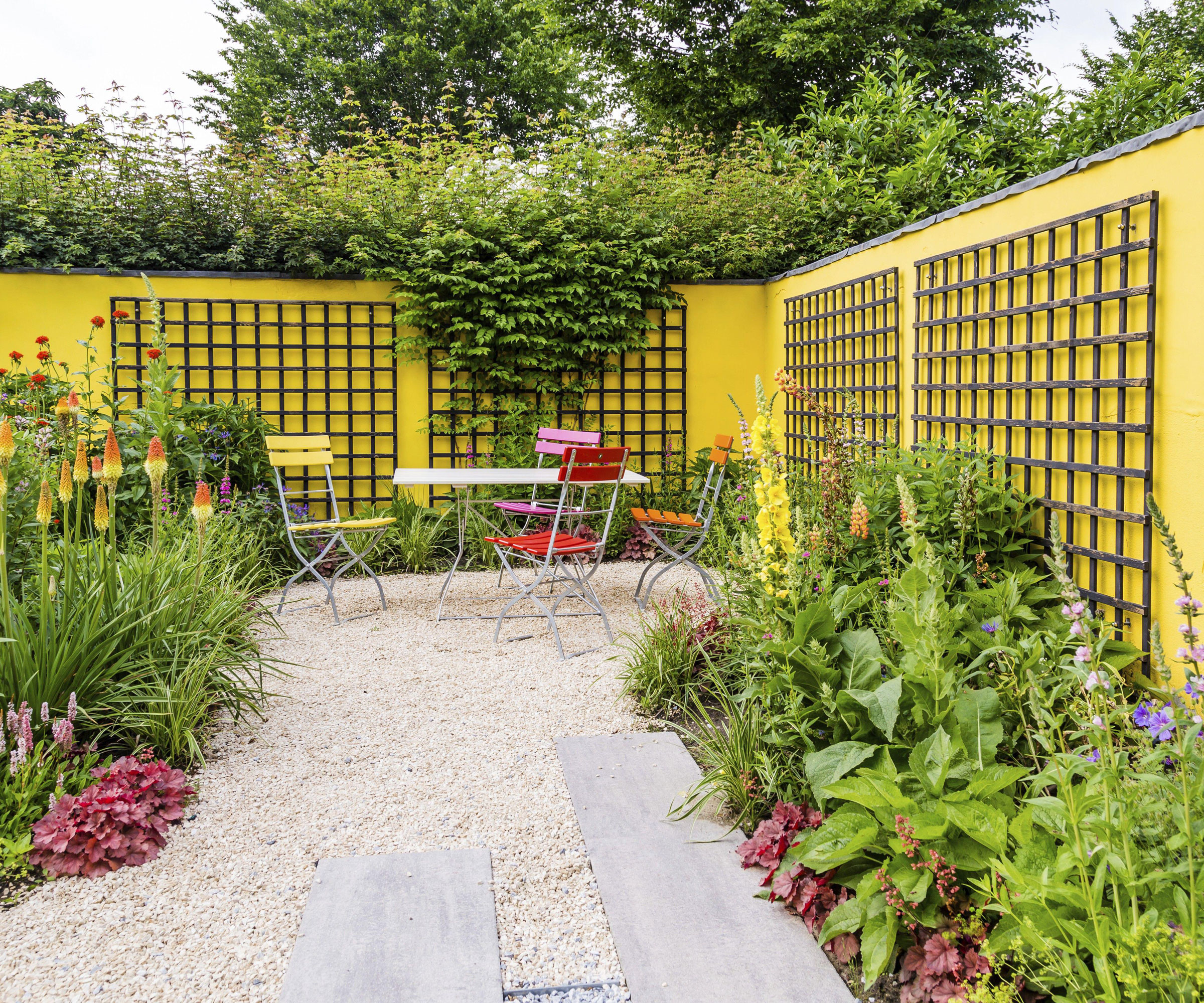 bright yellow garden walls with trellis, bistro set, flowerbeds with planting, pathway and gravel landscaping
