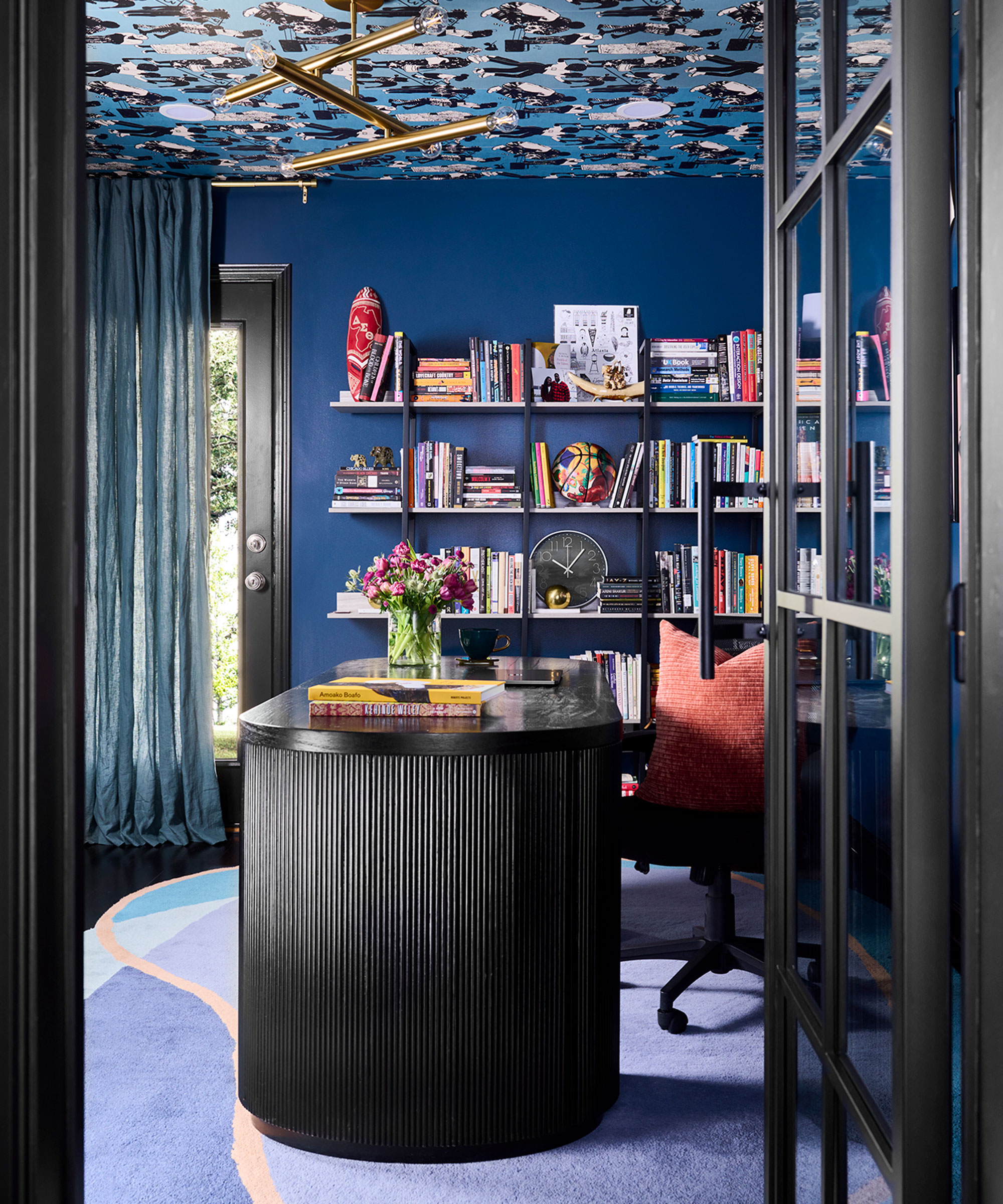 royal blue home office with black desk and wall of book shelves