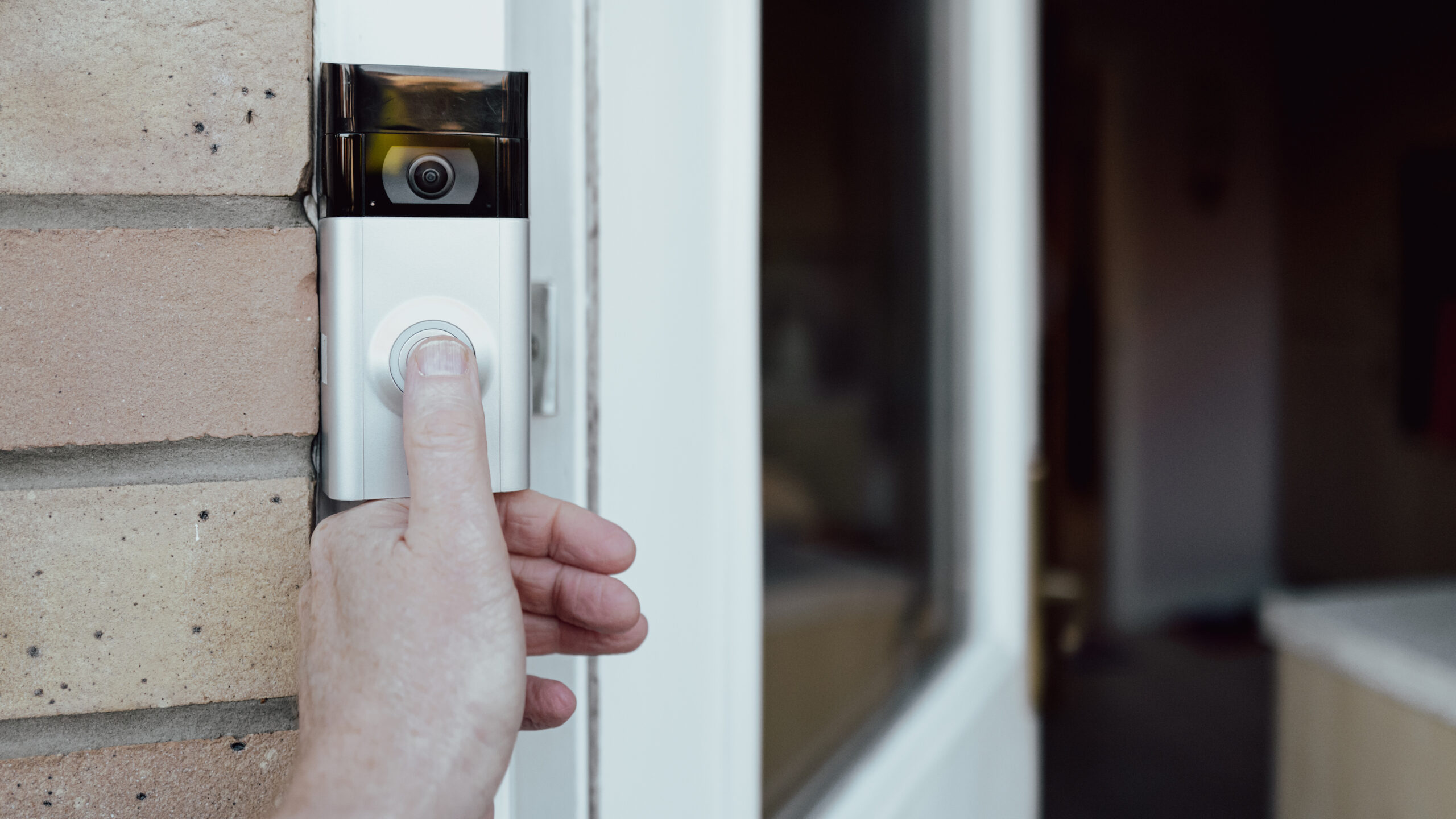 Person’s hand pressing button to test video doorbell fitted alongside white door