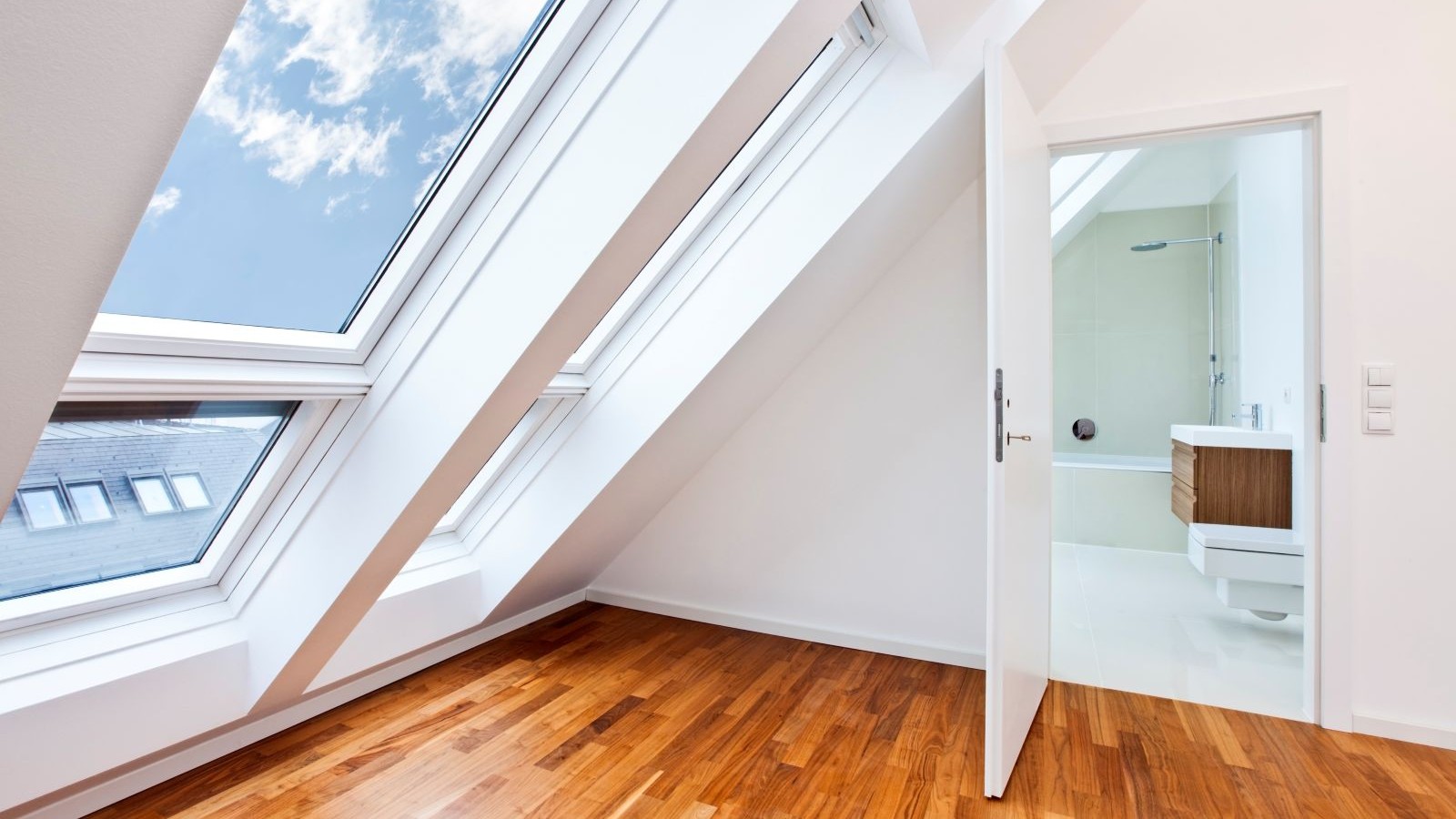 A loft conversion space with a wooden floor and sloped roof window and a white door leading into a bathroom