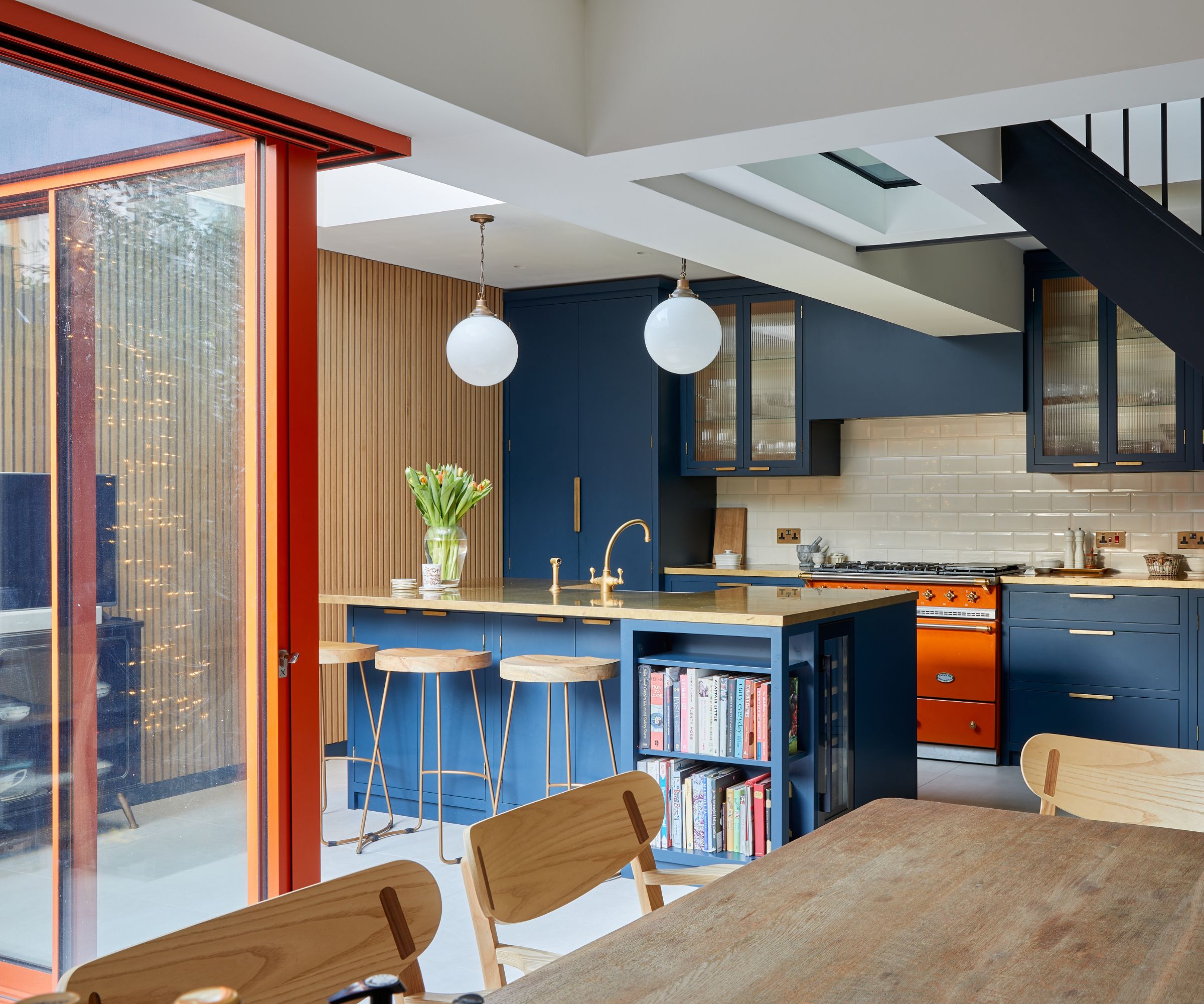 Contemporary kitchen with orange-framed sliding doors, navy cabinetry and brass details, creating a vibrant and stylish open-plan space.
