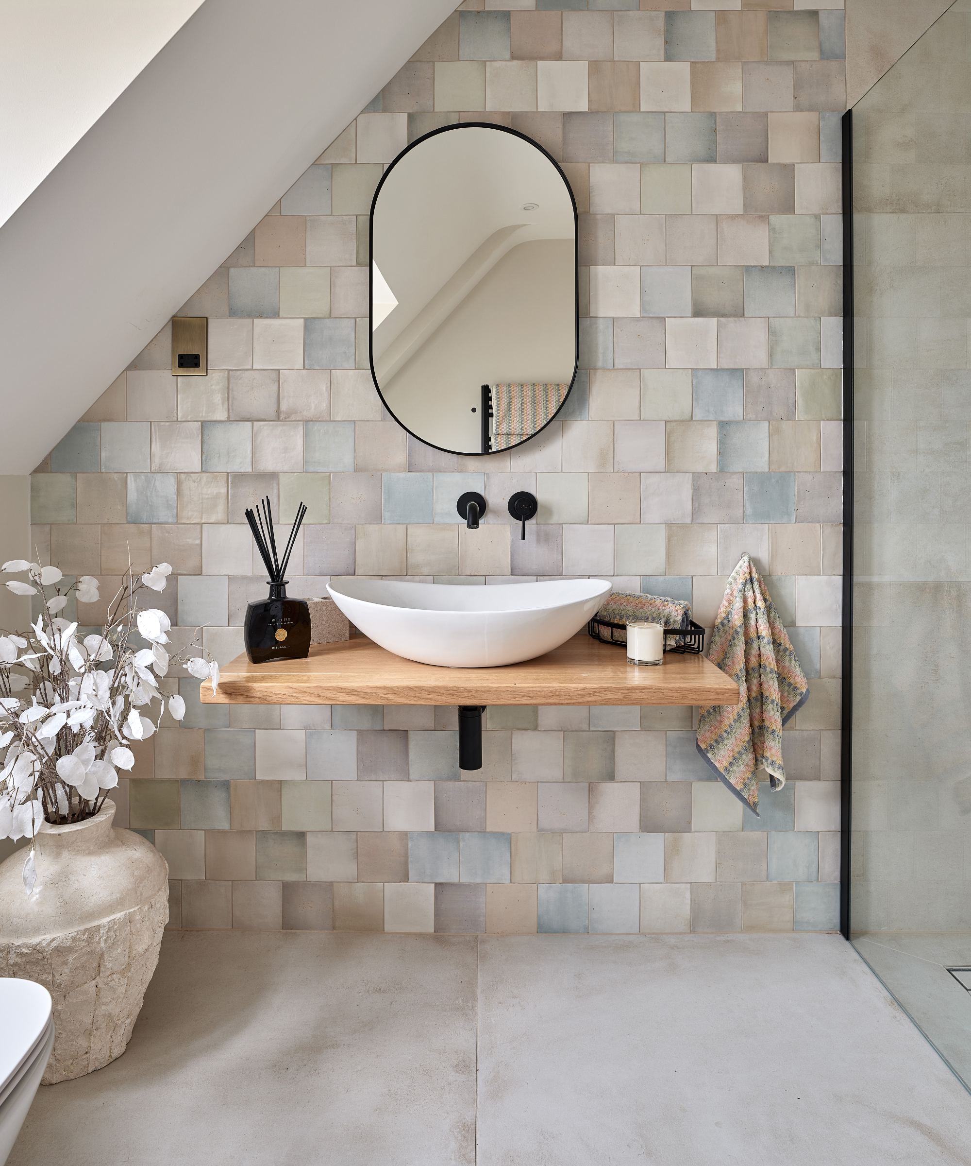 tiled bathroom with large floor tiles and smaller wall tiles, floating wooden shelf with countertop sink and mirror above