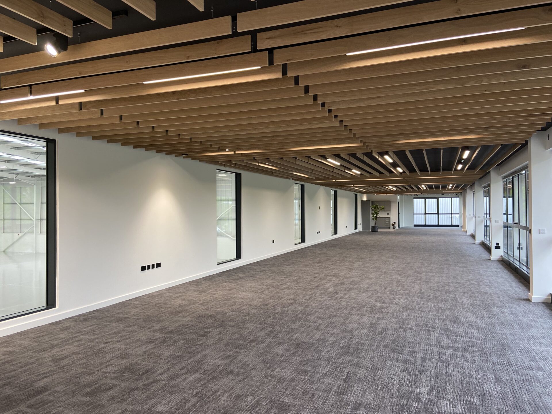 Inside of a logistics building. It has timber beams on the ceiling, no furniture and a few windows.