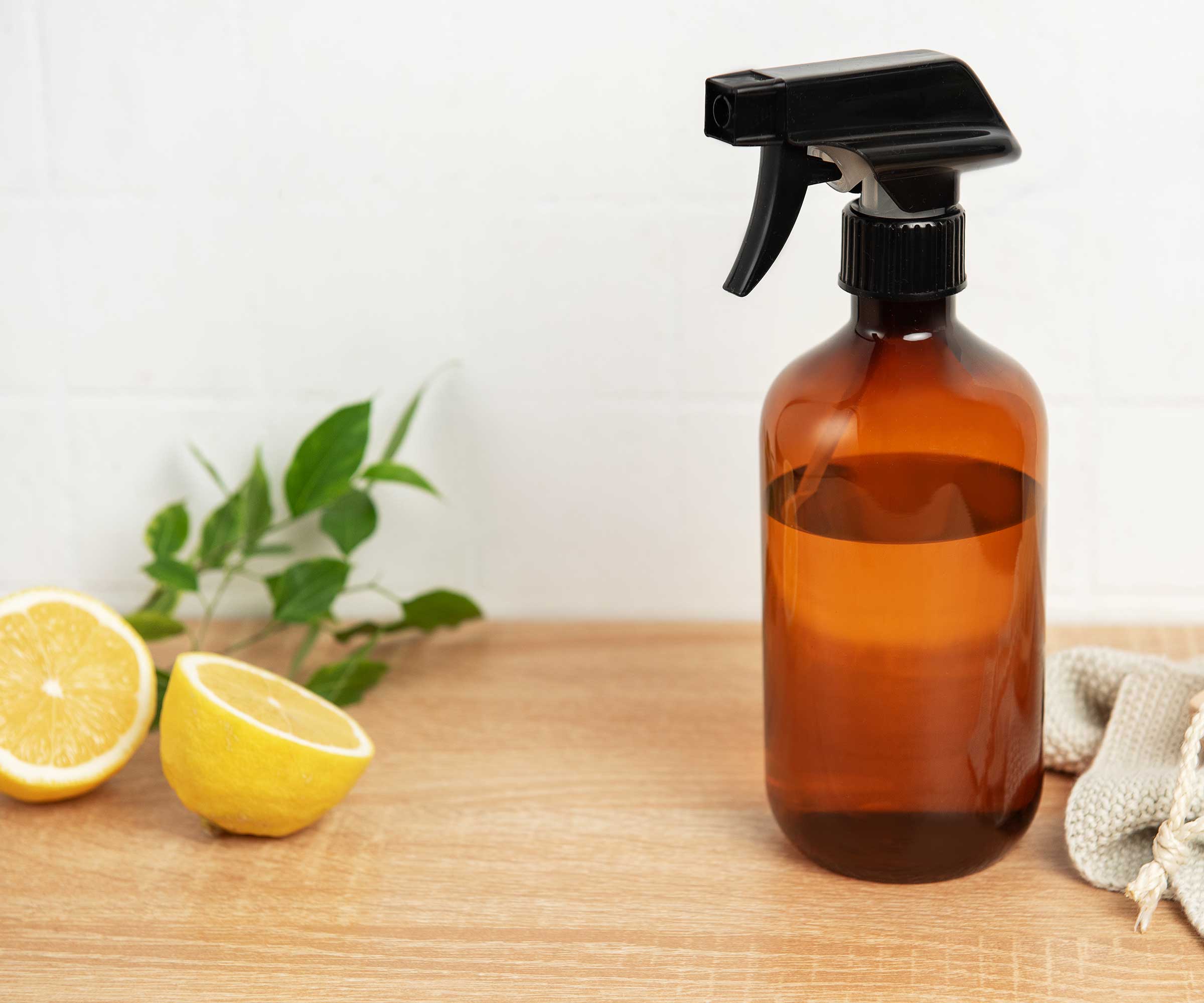 homemade cleaning and pest spray in a brown glass bottle next to a freshly sliced lemon