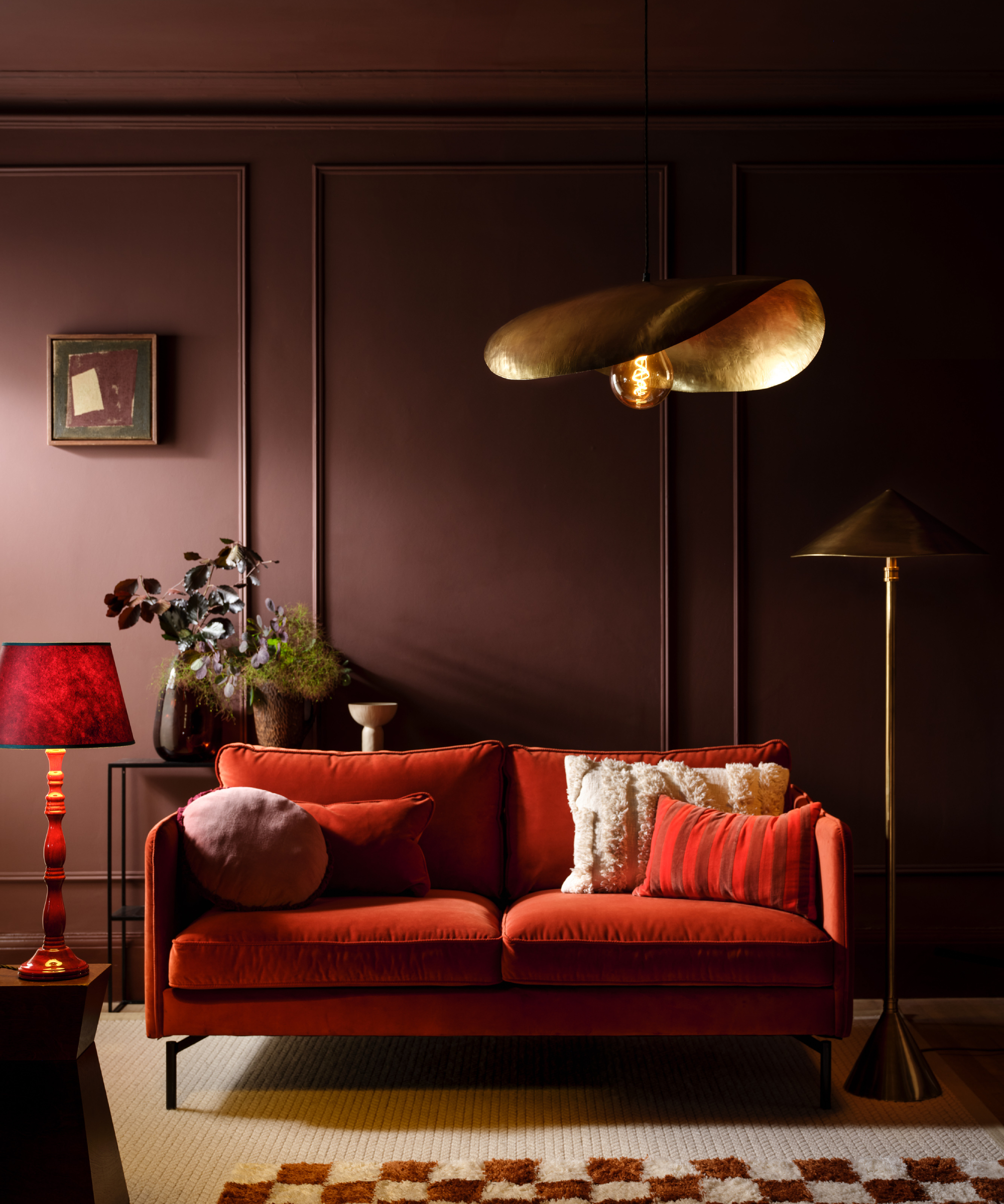 large matt gold pendant over red sofa in colour drenched living room