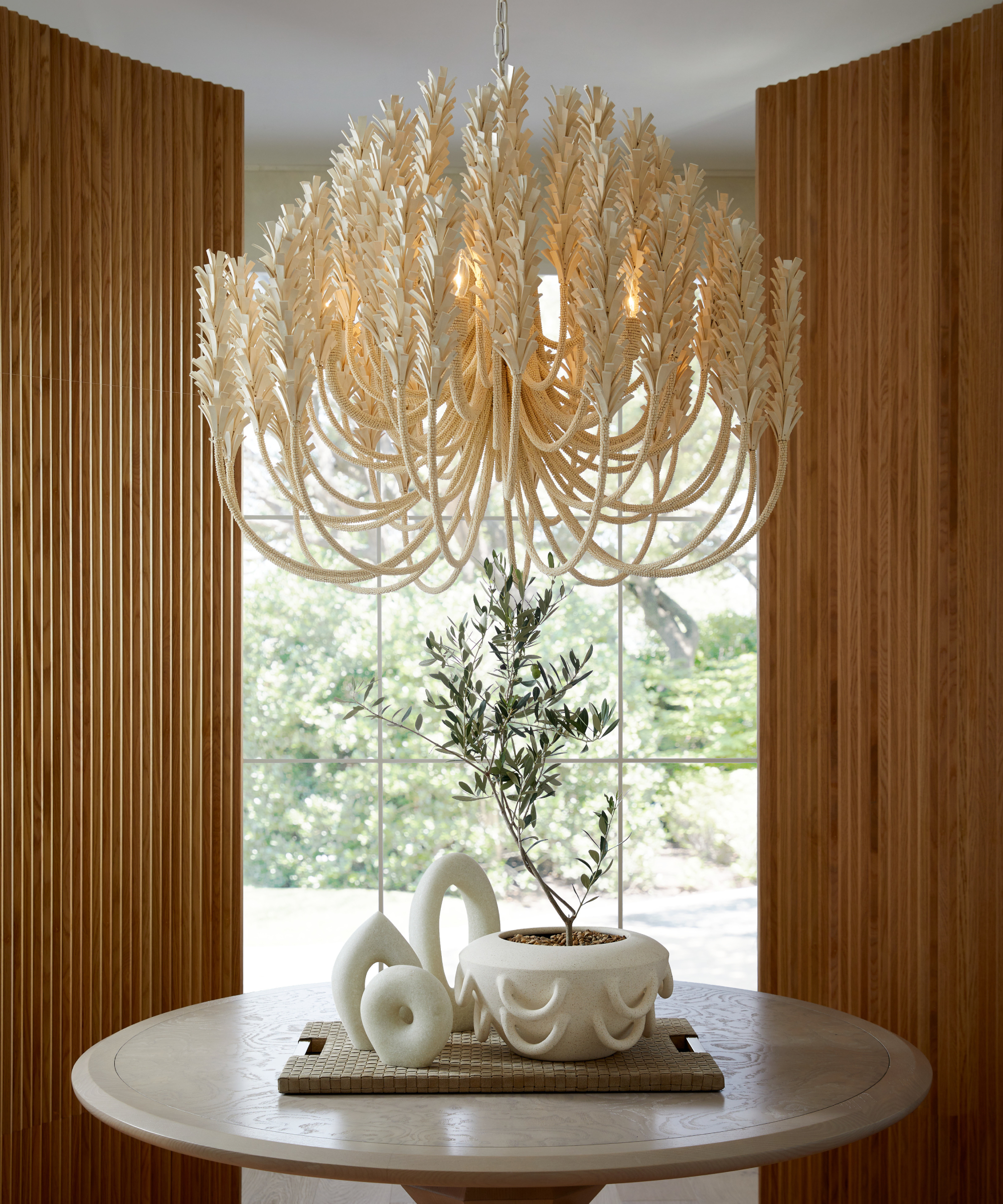 modern cream plantlike chandelier above table in space with fluted wooden panelling and window out to garden