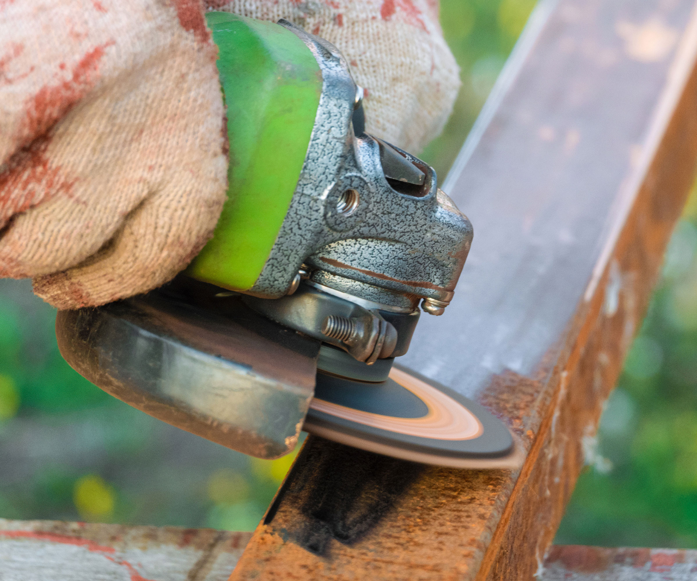 Gloved hand using angle grinder to clean rust off metal post