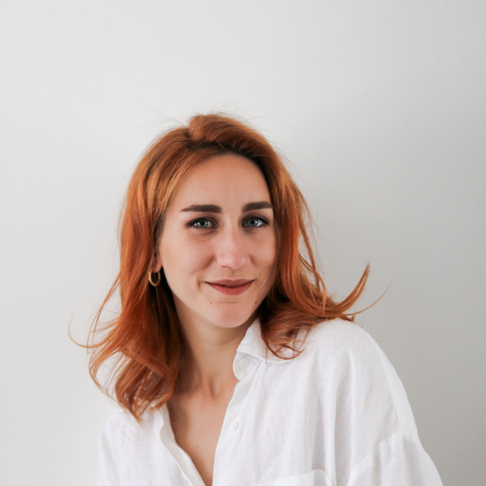 headshot of Marta Balazs, a female interior designer with red hair and blue eyes wearing a white shirt