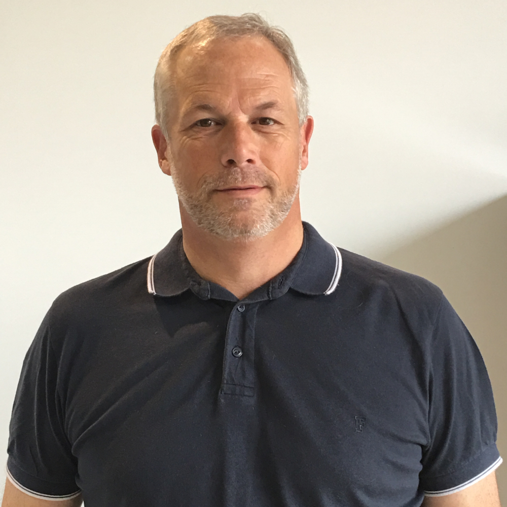 man with grey hair, short beard and moustache wearing navy polo shirt with white trim