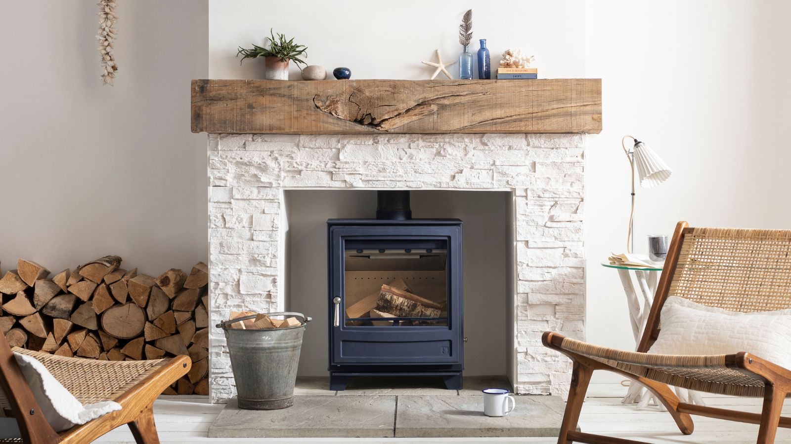 A contemporary coastal style living room with a whitewashed fireplace and black log burning stove with a pale oak beam above it