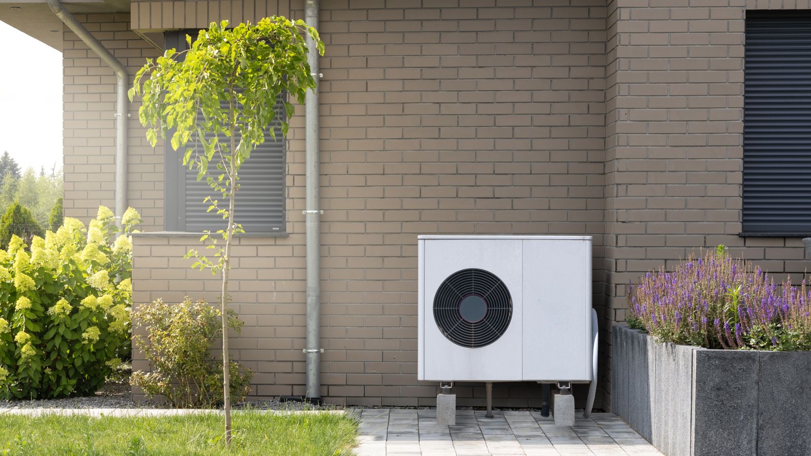 Modern heat pump system installed on the exterior of a building with plants and flowers.
