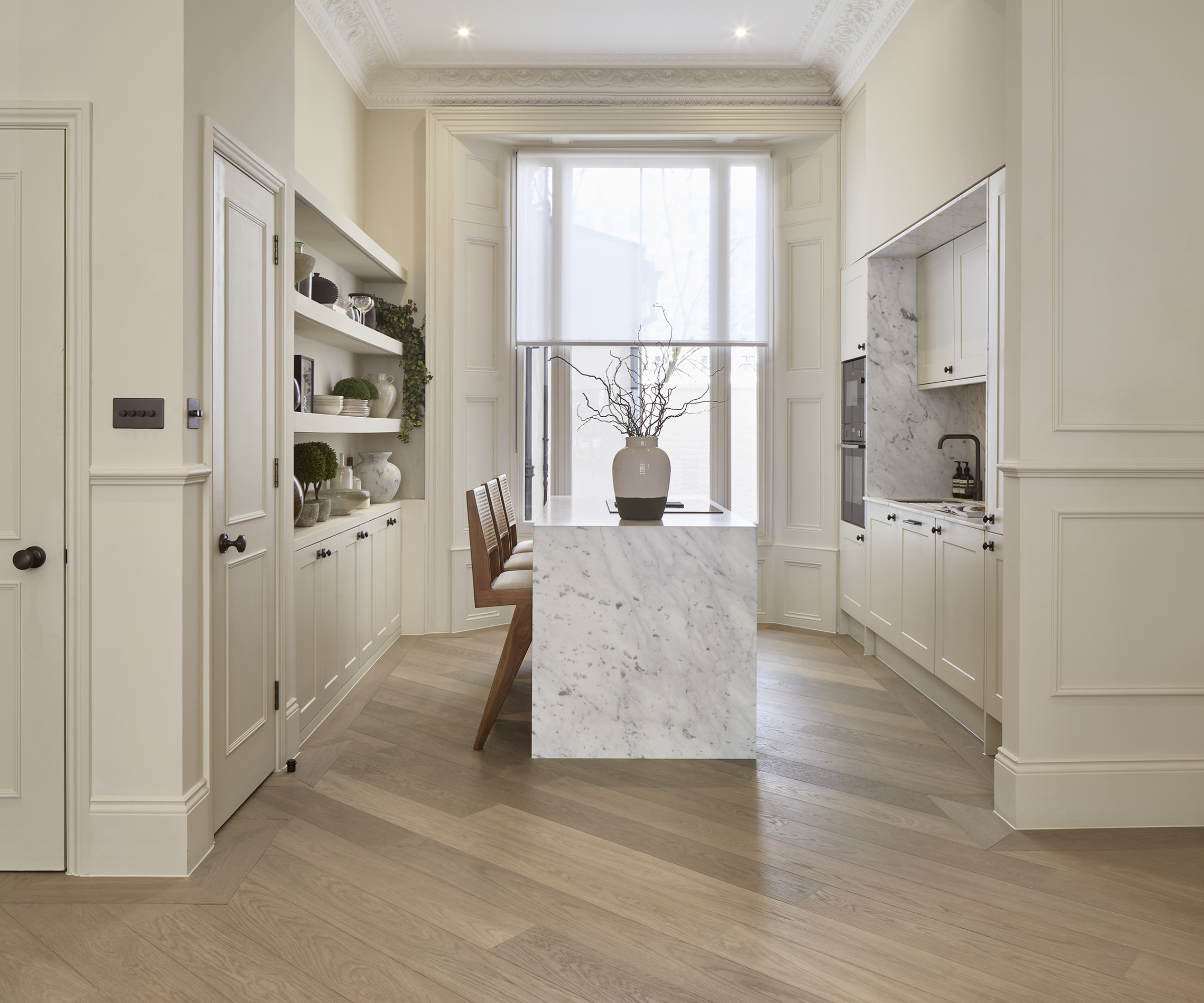 kitchen with light wooden flooring, off white units, large window and waterfall edged kitchen island with marble finish