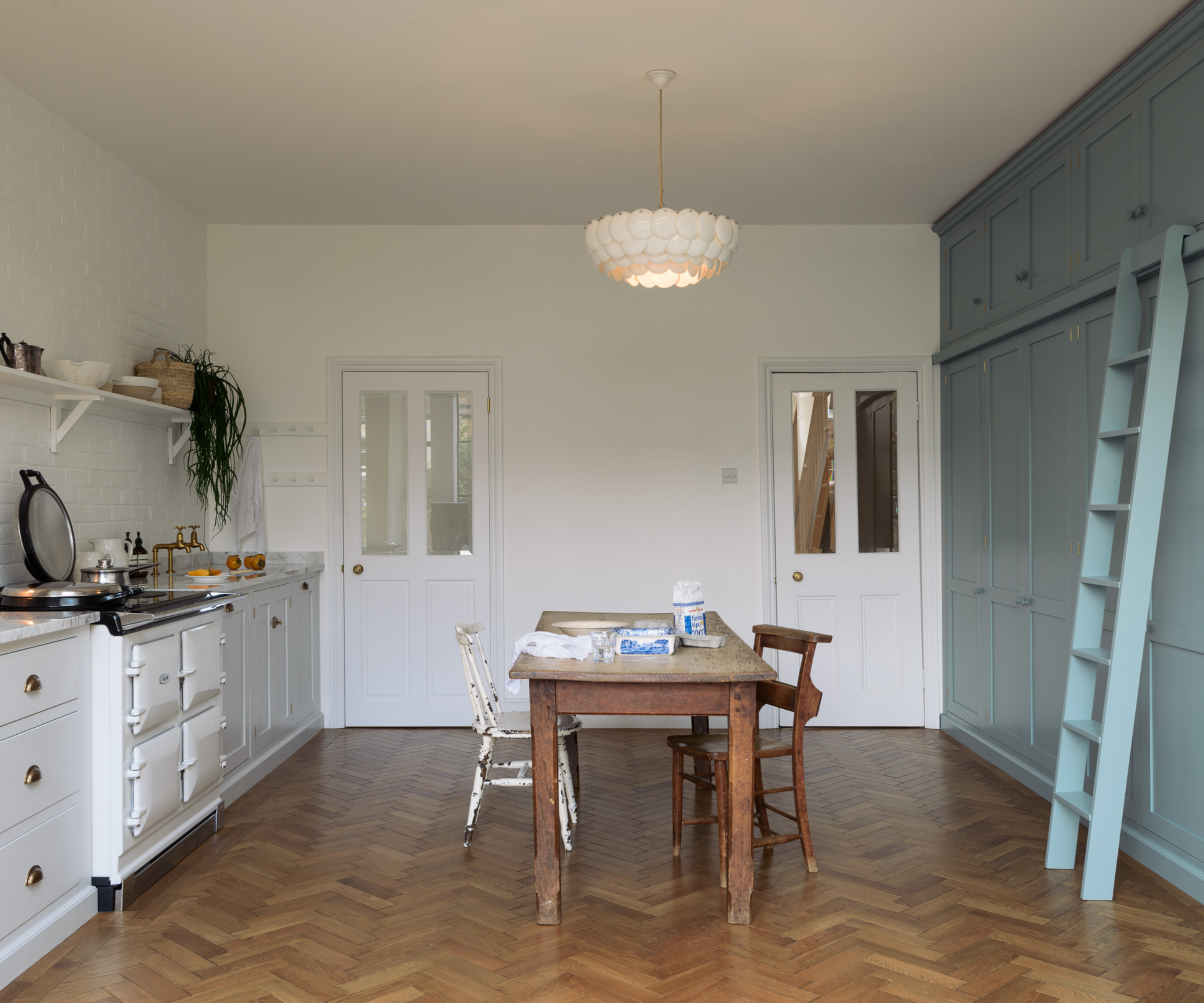 kitchen with white units one side, blue floor to ceiling cabinets and ladder on the other side, wooden floor and dining table in middle of room