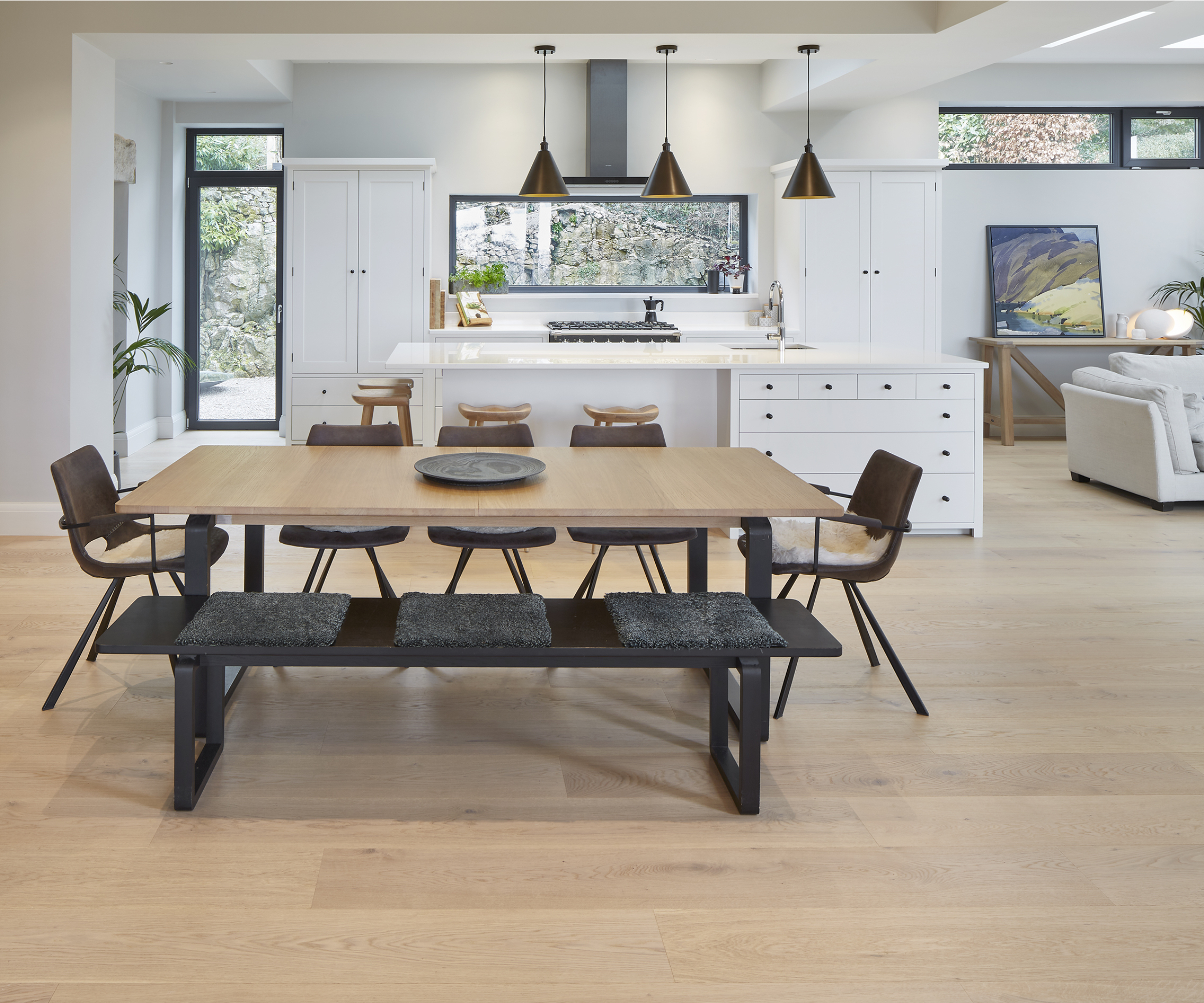 open plan kitchen diner and living room with white units, large wooden table with black chairs, white sofas and wooden floor