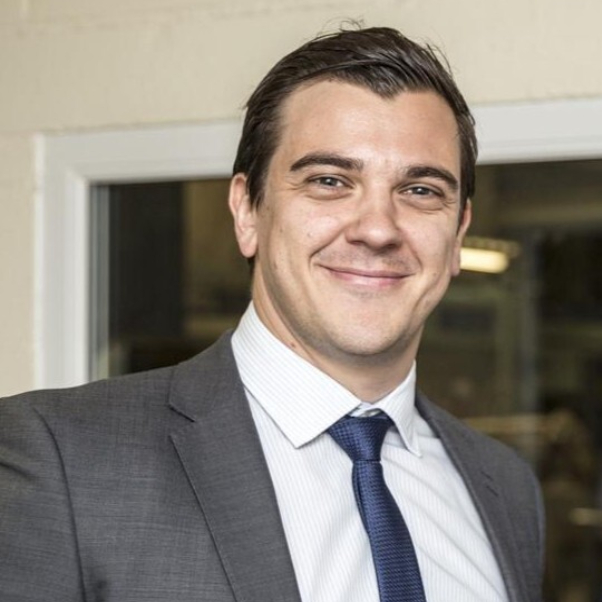 male with short dark hair wearing white shirt, grey suit and blue tie
