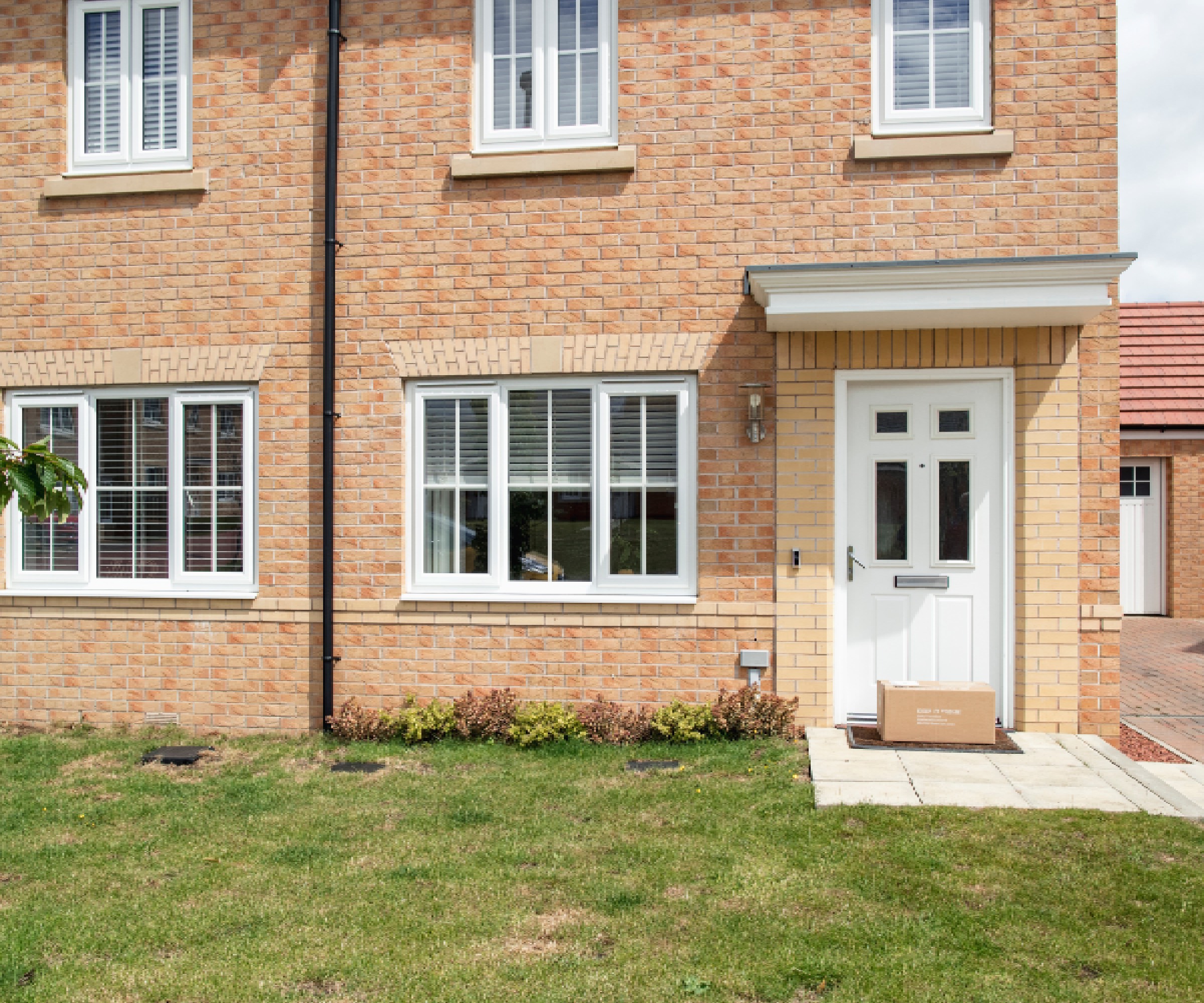 A wide-view shot of a residential building in Northeastern, England. A home delivery Box is at the front doorstep.