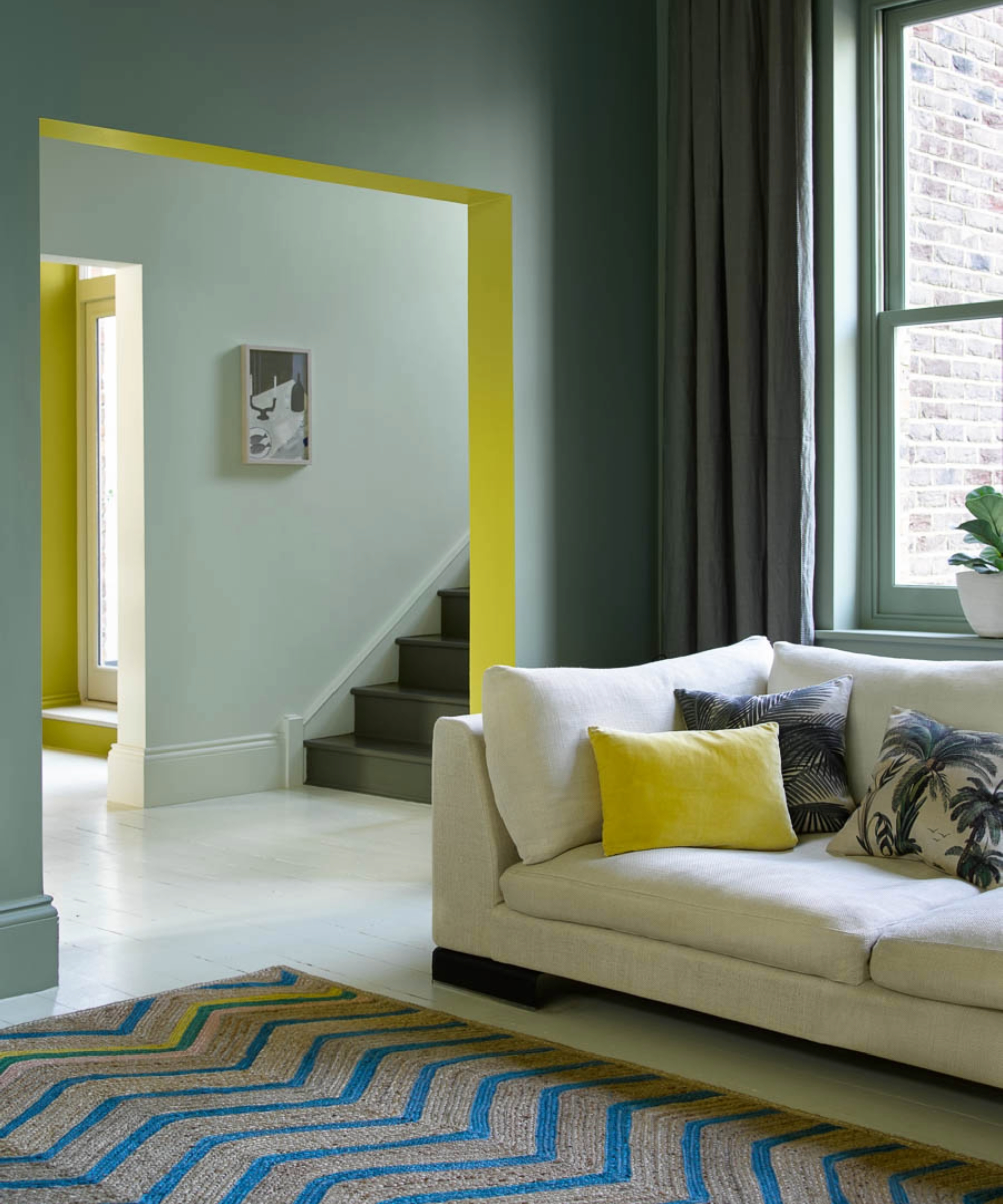 Green living room with pops of yellow in the archway and cushion