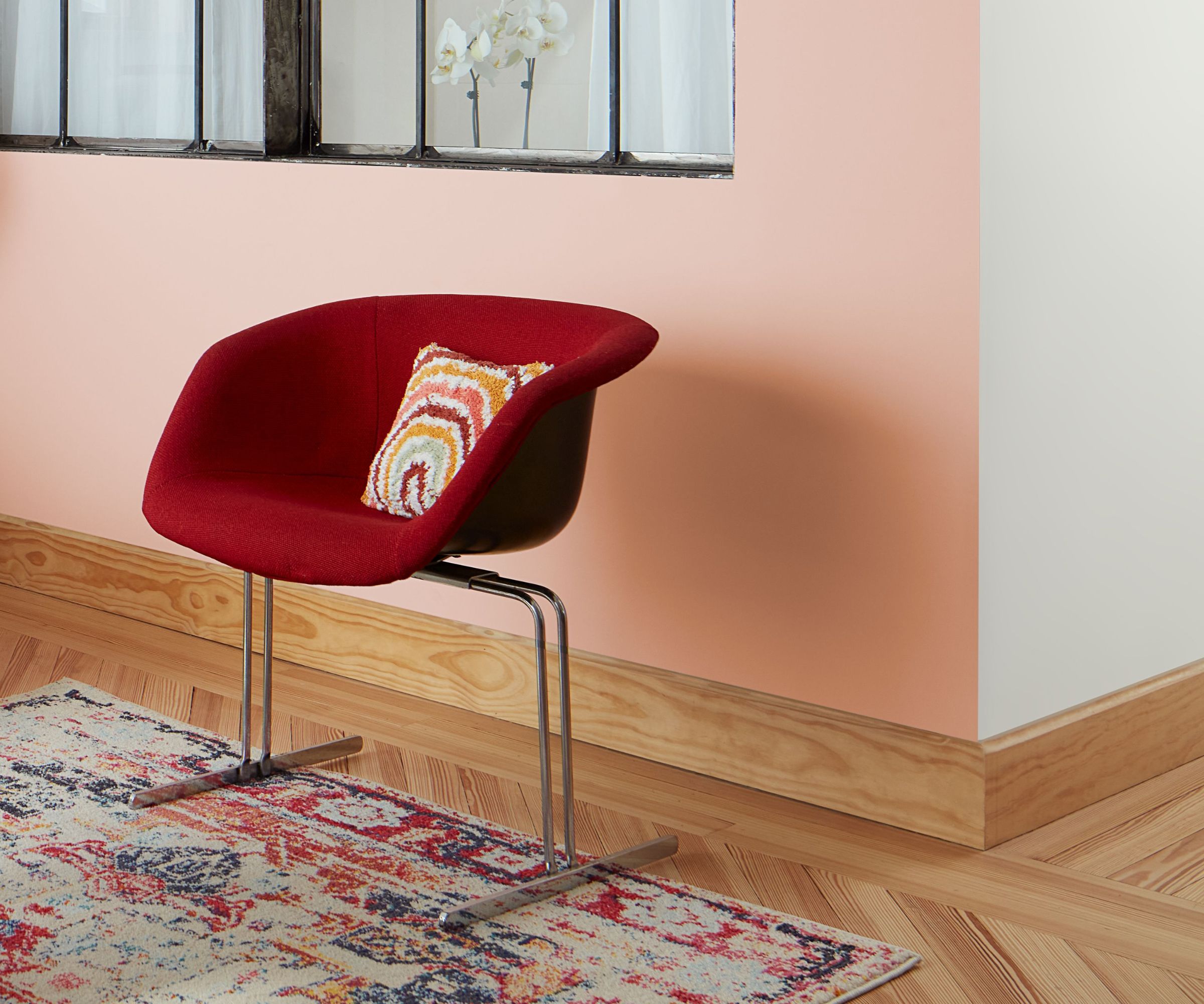 A mid century interior with a red armchair, wooden skirting and a colourful rug