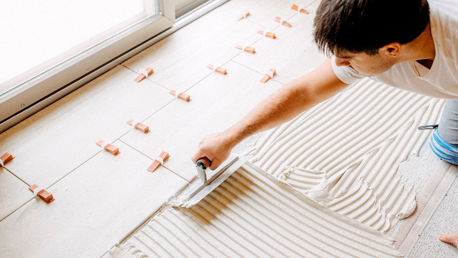 Man spreading tile adhesive with a notched trowel onto wooden floor with cement backer board