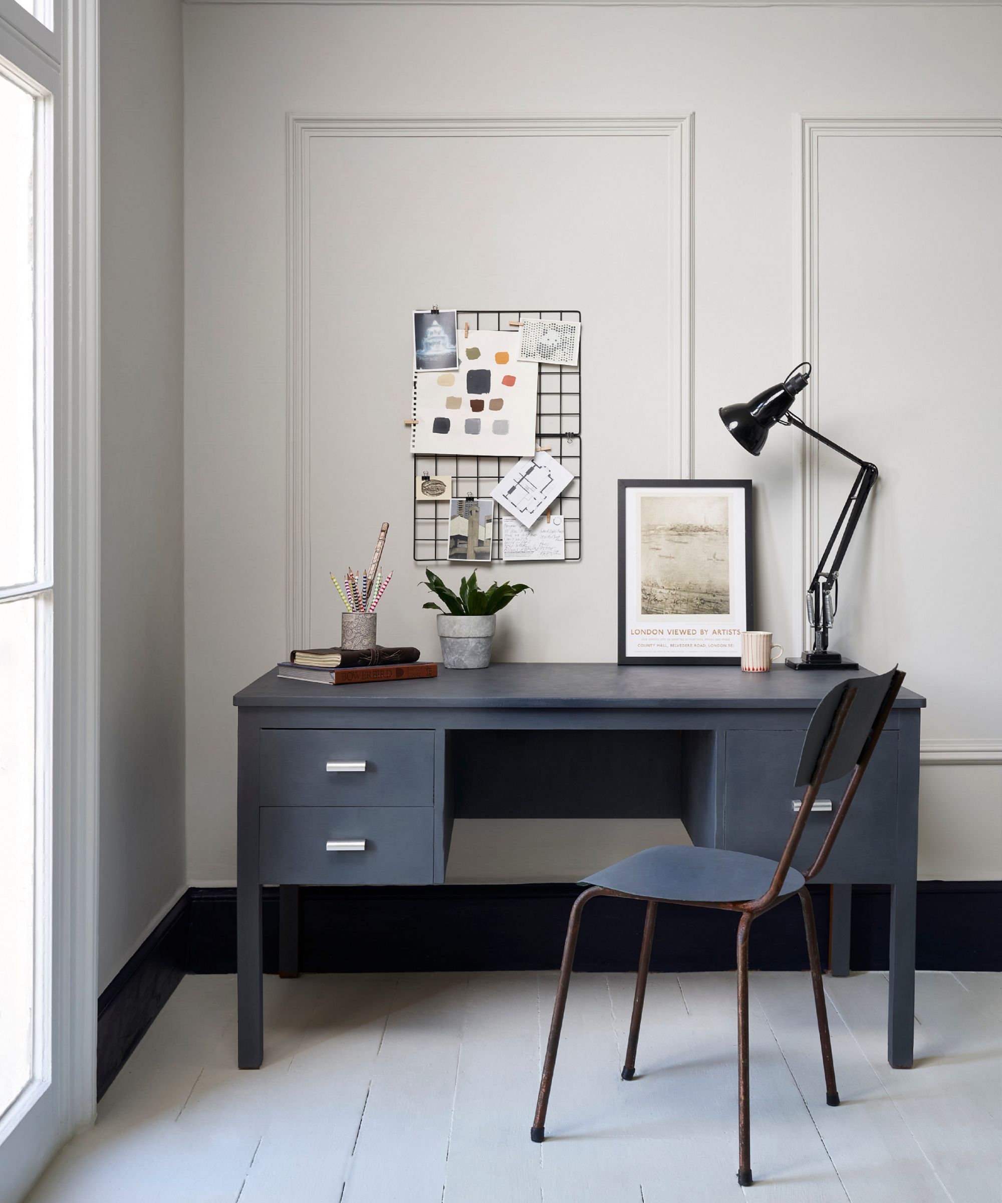 A minimalist home office with pale grey walls, a charcoal desk, and a simple metal chair. Natural light and pared-back styling create a calm, focused workspace.