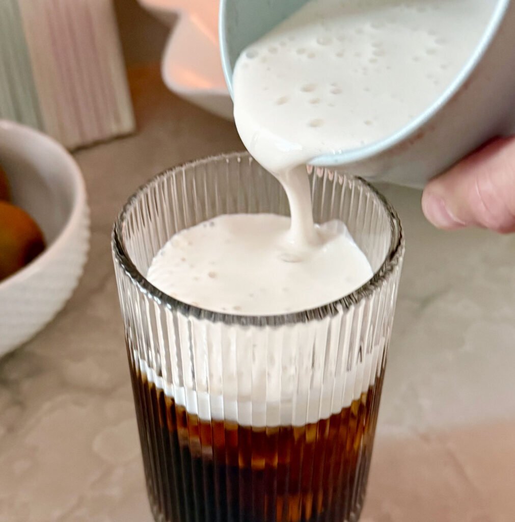 Pouring homemade cold foam creamer over cold brew coffee