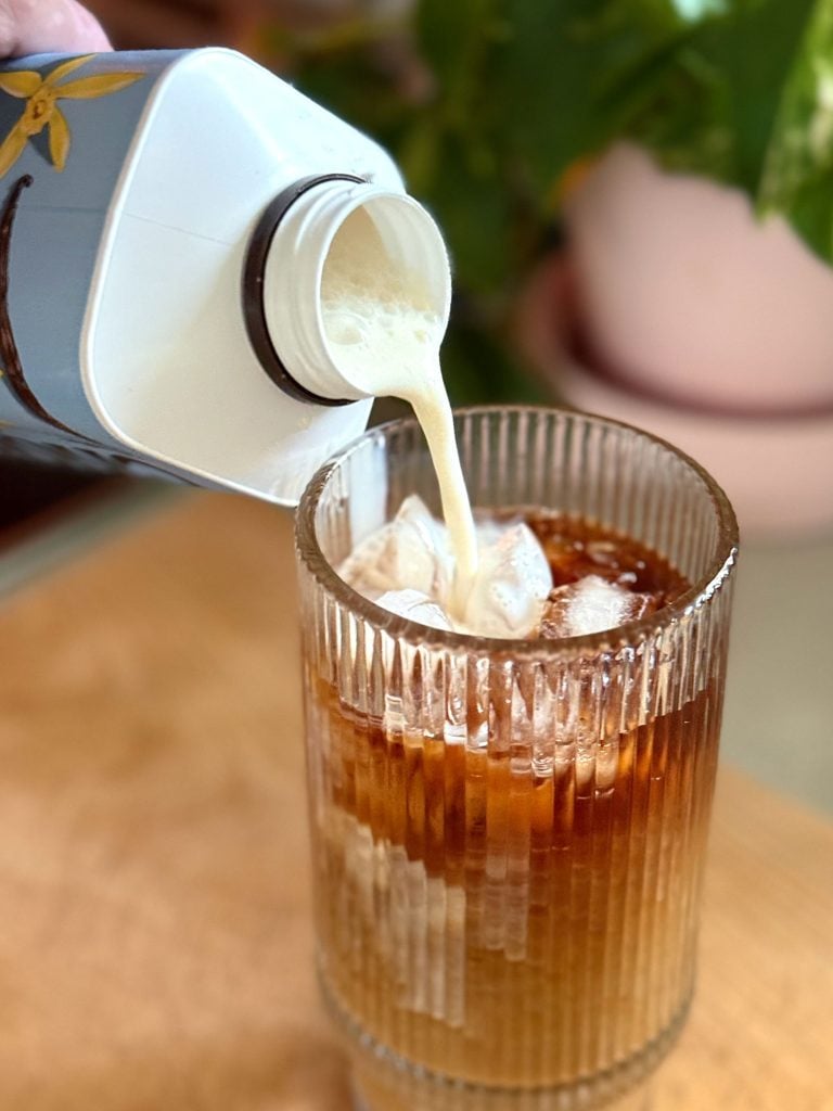 Pouring Creamer Into Glass of Iced Cold Brew Coffee Made At Home